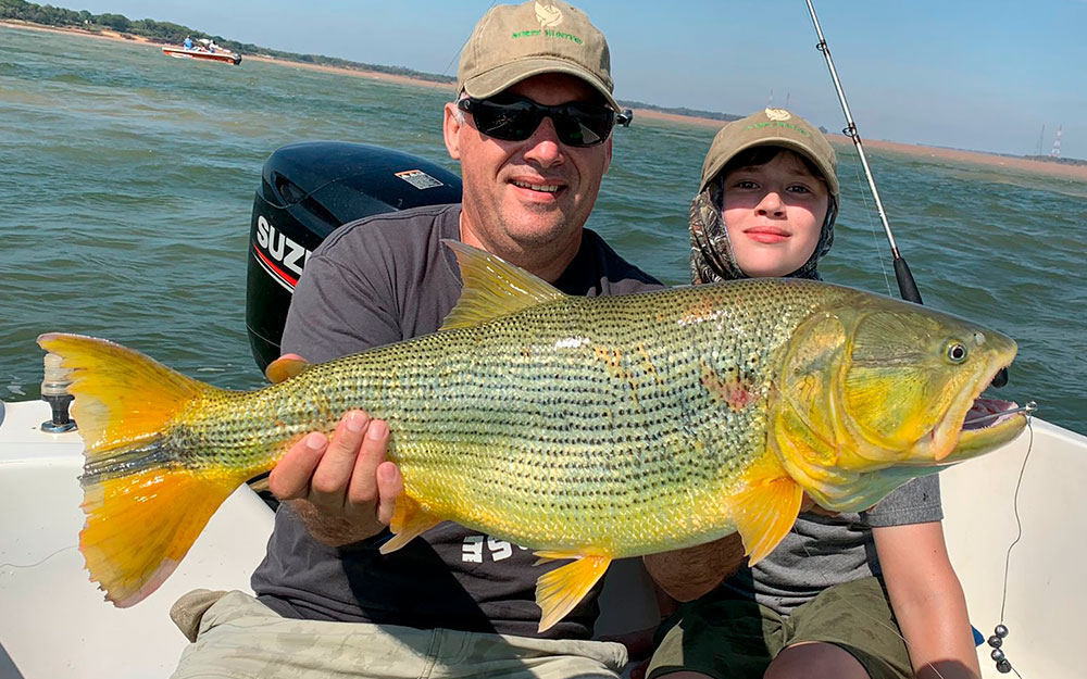 An adult and child holding a golden dorado from a boat