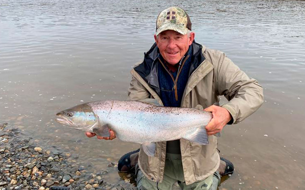 An angler holding a large trout beside the water